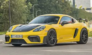 Żółty Porsche Cayman GT4 RS z czarną maską i spojlerem, gotowy do jazdy po miejskich ulicach.
