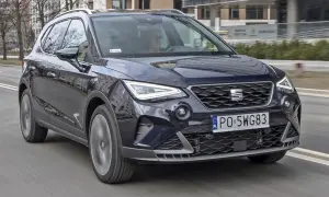 Ciemnoniebieski Seat Arona w ruchu miejskim. Kierowca w okularach. Wiele pozytywnych seat arona opinie potwierdza jego miejski charakter.