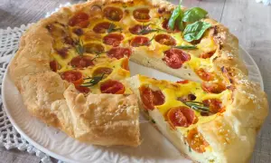 Une quiche ricotta aux tomates cerises et romarin, garnie de graines de sésame, sur une assiette blanche.