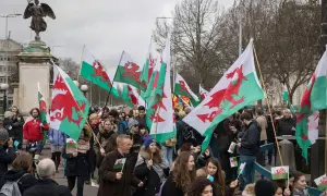 Grupa ludzi maszeruje z walijskimi flagami z czerwonymi smokami.