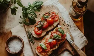 Två bitar bruschetta med mozzarella, färska tomater och basilika på en träskärbräda. En flaska olivolja och en skål med flingsalt syns bredvid.