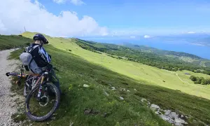 Ciclista con mountain bike ammira il panorama del lago di Garda dal Monte Baldo.
