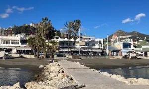 Paseo marítimo en la playa pedregalejo como llegar. Palmeras, restaurantes y montañas al fondo bajo un cielo azul.