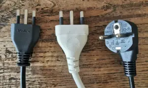 Trzy wtyczki elektryczne, w tym dwie z trzema bolcami, typowe dla gniazdek we Włoszech, leżą na drewnianym blacie.
