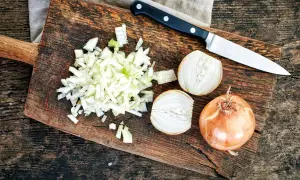 Cipolla cruda digeribile, tagliata finemente su un tagliere di legno, accanto a una cipolla intera e a metà. Un coltello è pronto all'uso.
