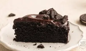 Ein Stück saftiger Oreo Kuchen mit glänzender Schokoladenglasur und zerbröselten Keksen obendrauf.