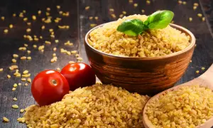 Miseczka kaszy bulgur, pomidory i drewniana łyżka. Czy kasza bulgur jest zdrowa? Tak, to bogactwo błonnika i witamin.