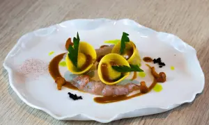 Trois raviolis italiens dorés, garniture de crevettes, champignons et sauce brune sur une assiette blanche ondulée.