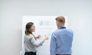 Kvinna förklarar en modell på whiteboarden för en man. Diskussionen kan handla om skillnad mellan befattningsbeskrivning och arbetsbeskrivning.