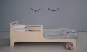 Drewniane łóżeczko dla lalek z poduszką i misiem, przykryte szarym kocem.