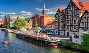 Nad rzeką w Bydgoszczy, jednym z największych miast w Polsce, cumuje statek. W tle zabytkowe kamienice i nowoczesna architektura.