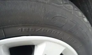Gros plan sur un pneu rechapé avec inscription 185/65R15. La jante est visible en bas.