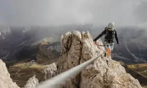 Kobieta na via ferrata polska pokonuje skalną grań, w tle górzysty krajobraz z krętymi drogami.
