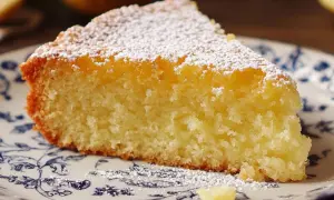 Tranche de fondant citron mascarpone saupoudrée de sucre glace, sur une assiette ornée de motifs bleus.