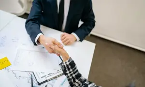 Accordo per vendere immobile: il procuratore valuta i rischi. Due persone si stringono la mano su un tavolo con grafici.
