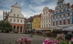 Kolorowe kamienice na Rynku Staromiejskim w Szczecinie, z brukowanym placem i kwiatami w tle.
