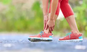 Kobieta w czerwonych legginsach trzyma się za bolesną kostkę w różowych butach sportowych.