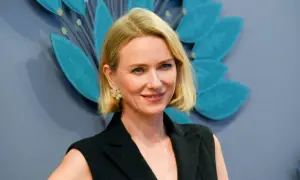 Uśmiechnięta Naomi Watts, znana z wielu filmów, w czarnej stylizacji i z kwiatową broszką.