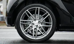 Błyszczące, czarne nadkole samochodu z felgą Brabus i oponą na mokrej nawierzchni.