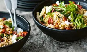 Zwei Schalen mit einem köstlichen nudelsalat mit getrockneten tomaten, Pinienkernen und Rucola, garniert mit Feta.