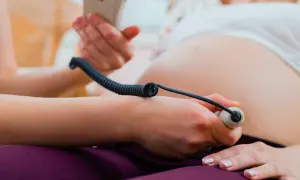 Gravid kvinna får sitt foster lyssnat på med doppler. Vårdgivaren håller instrumentet mot magen.