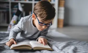 Niño con gafas azules concentrado en un libro abierto, aprendiendo a leer.