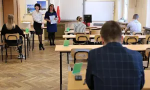 Uczniowie siedzą w ławkach, czekając na egzamin. Nauczycielki stoją z przodu, trzymając dokumenty. Ile trzeba mieć procent żeby zdać egzamin zawodowy?