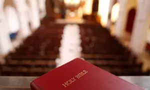 Czerwona Biblia leży na pierwszym planie, w tle widać rzędy pustych ławek w kościele. Szukasz odpowiedzi, jak przejść na protestantyzm?