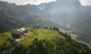 Holzhaus auf einem grünen Hügel, umgeben von majestätischen Bergen. Ein perfekter Ort für die Dachstein Sonnenrunde.