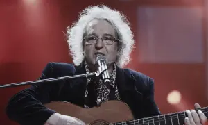 Zegarmistrz światła purpurowy, z burzą białych włosów, gra na gitarze i śpiewa przy mikrofonie.