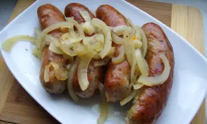 Biała kiełbasa pieczona w cebuli i musztardzie, podana na białym talerzu.