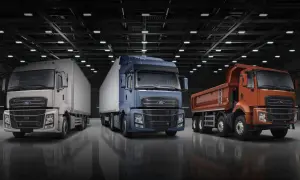 Trois camions Ford F-Line : un blanc avec remorque, un bleu avec remorque, et un orange benne basculante, alignés dans un entrepôt.