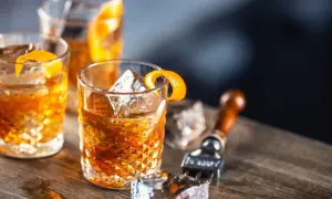 Tre old fashioned-drinkar med is och apelsinskal på ett träbord. En cocktailgaffel ligger bredvid.