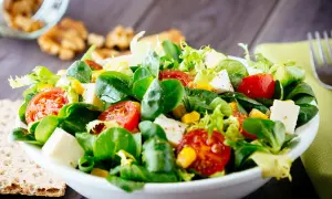 Ein bunter gemischter Salat mit Tomaten, Mais und Feta-Käse, serviert in einer weißen Schüssel auf einem Holztisch.