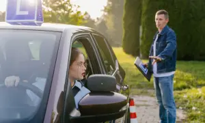 Młoda kursantka za kierownicą samochodu z literą "L", instruktor obok z tabliczką. Czy kurs na prawo jazdy przepada?