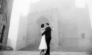 Sposi si baciano davanti a un antico arco in pietra, immersi nella nebbia. Dettagli matrimonio suggestivi.
