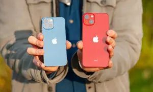 Dwie ręce trzymają dwa telefony: niebieski i czerwony iPhone 13 mini. Oba mają charakterystyczny aparat.