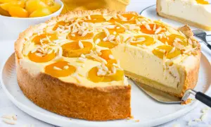 Ein köstlicher Landfrauen Aprikosenkuchen mit Mandelsplittern, frisch angeschnitten. Daneben eine Schüssel mit Aprikosen.