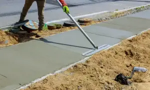 Robotnik wygładza świeży beton C20/25 na chodniku. Właściwe proporcje składników zapewniają trwałość.
