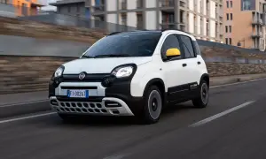 Biały Fiat Panda 3 z żółtym lusterkiem jedzie po drodze.