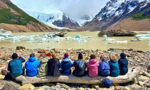 Gruppe sitzt auf Baumstamm vor Gletschersee mit Eisbergen. Tolle Eberhardt Travel Erfahrungen in Patagonien.