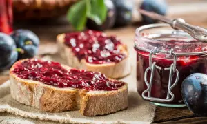 Zwei Scheiben Brot mit Zwetschgenmarmelade mit Zimt, daneben ein Glas der Marmelade und frische Zwetschgen.