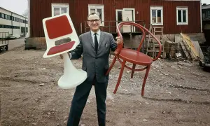 Man i kostym håller en röd stol och en vit stol med röd sits. Kanske en tidig idé för Ingvar Kamprad utbildning i möbeldesign.