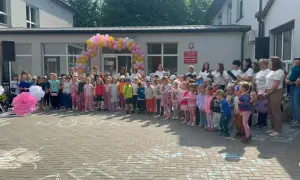 Dzieci i dorośli stoją przed budynkiem ozdobionym balonami. Widać biała podlaska atrakcje dla dzieci, takie jak wielkie papierowe kwiaty i rysunki na chodniku.