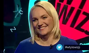 Uśmiechnięta blondynka w niebieskiej sukience. W tle wizji prowadzący, litery i cyfry.