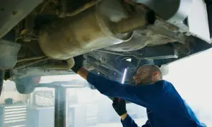 Mechanik w niebieskim kombinezonie oświetla latarką p0420 podwozie samochodu.