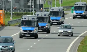 Konwój pojazdów uprzywilejowanych: policyjne furgonetki i samochód osobowy jadące autostradą.