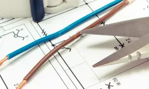 Niebieski i brązowy kabel leżą na schemacie elektrycznym. Czy czerwony kabel to plus czy minus? Nożyczki zbliżają się do przewodów.