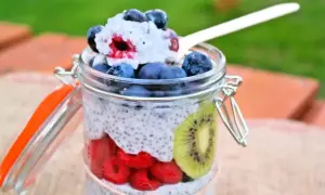 Pudding chia z owocami w słoiku: maliny, borówki, kiwi i łyżka z deserem.
