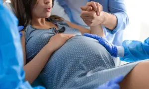 Mujer embarazada en trabajo de parto, con su pareja sosteniendo su mano y personal médico asistiendo. Se enfoca en el vientre, sugiriendo el momento de cómo provocar el parto.